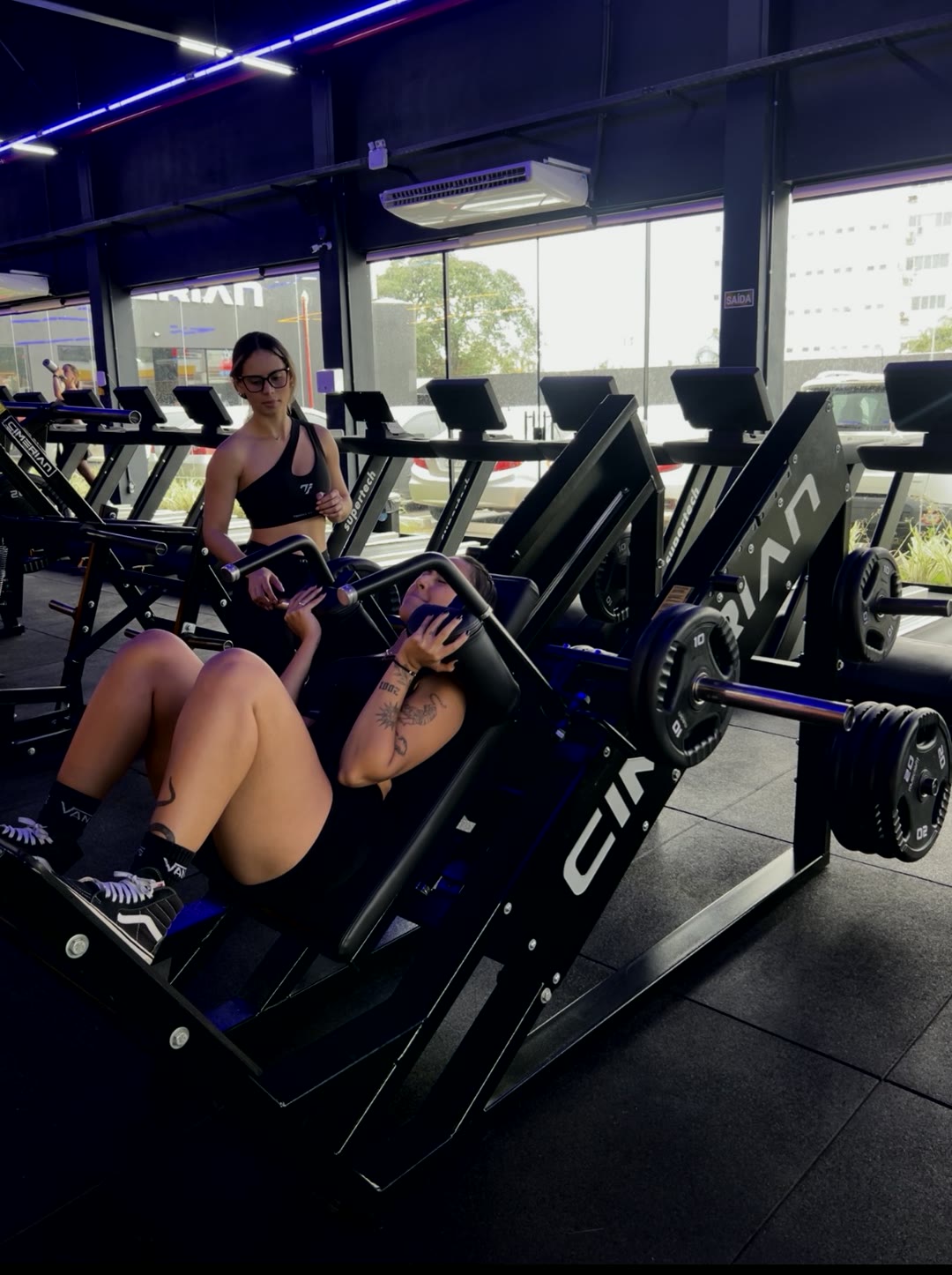 Aluna treinando no leg press com acompanhamento